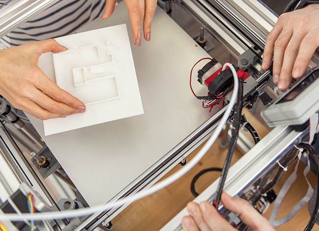 Zwei Personen halten ein Modell aus 3D-Filament über einem 3D-Drucker